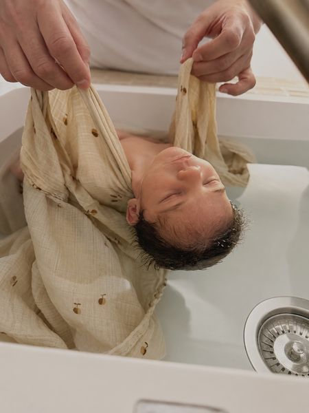 Nouveau-né lové dans un lange en coton pendant le bain